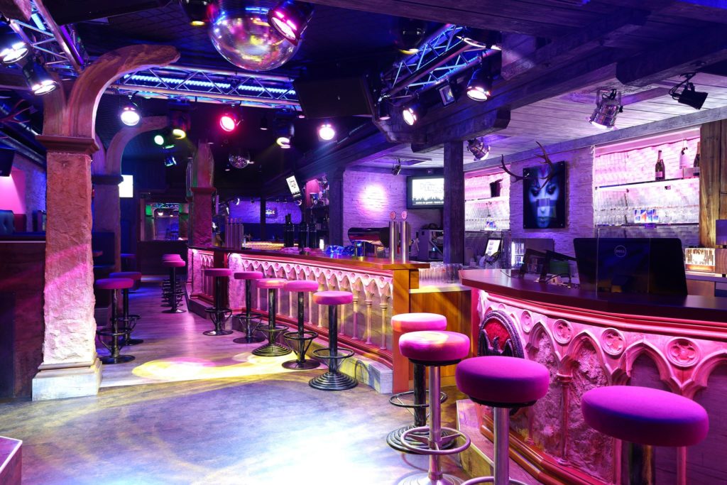 Die Bar der Disco Fuggo in pinkem und violettem Licht, mit Discokugel und Barhockern