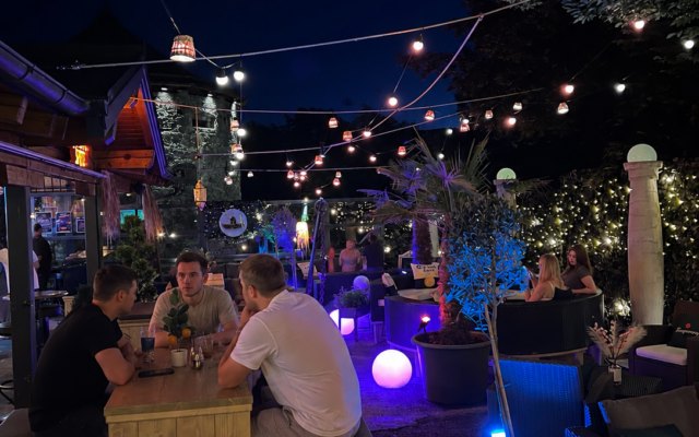 Gäste sitzen abends im Fuggo Garden unter Lichterketten